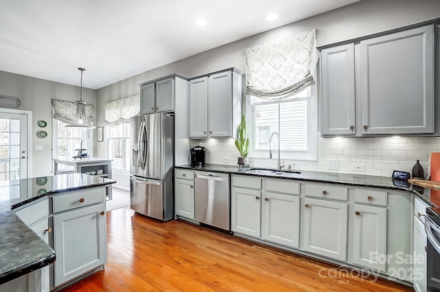 kitchen with appliances with stainless steel finishes, sink, gray cabinetry, hanging light fixtures, and light hardwood / wood-style floors