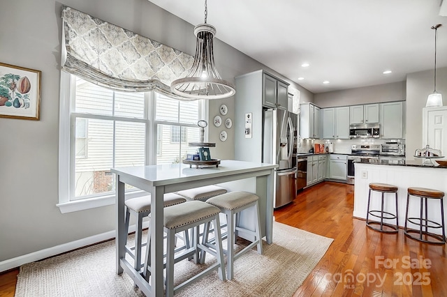 kitchen with pendant lighting, gray cabinets, a breakfast bar, and appliances with stainless steel finishes