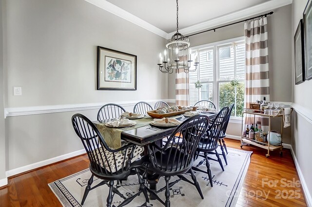 dining area with wood-type flooring, ornamental molding, and a chandelier