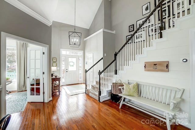 foyer entrance with an inviting chandelier, hardwood / wood-style floors, ornamental molding, and high vaulted ceiling