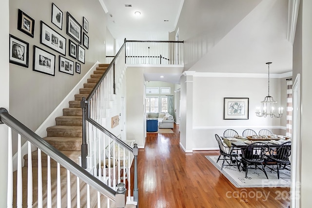 staircase featuring an inviting chandelier, wood-type flooring, ornamental molding, a towering ceiling, and decorative columns