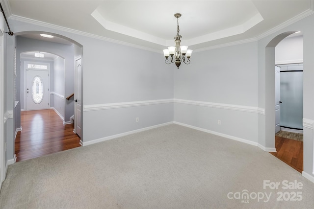 carpeted spare room with an inviting chandelier, ornamental molding, a raised ceiling, and baseboard heating