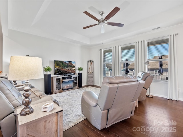 living room featuring dark hardwood / wood-style flooring, a raised ceiling, and ceiling fan