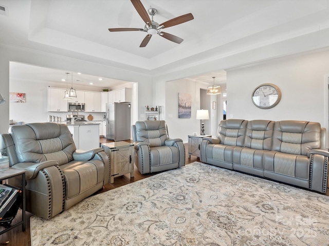 living room with a raised ceiling, ceiling fan, ornamental molding, and light wood-type flooring