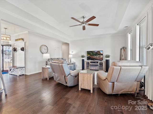 living room featuring ceiling fan with notable chandelier, dark wood-type flooring, and a raised ceiling