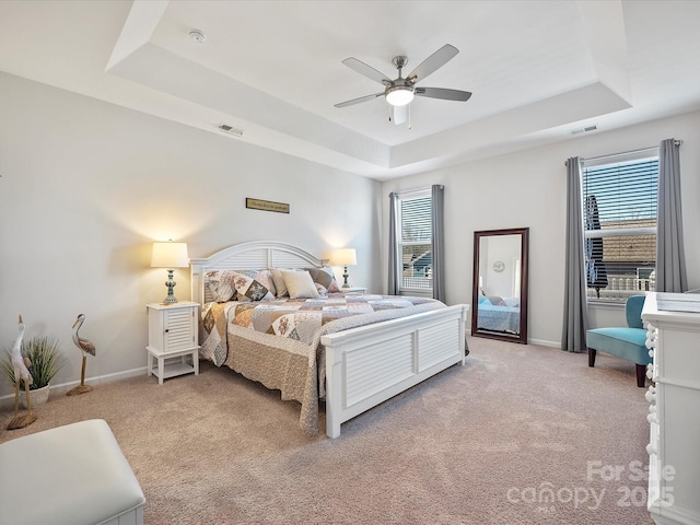 carpeted bedroom featuring multiple windows, ceiling fan, and a tray ceiling