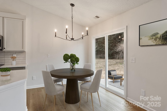 dining space featuring plenty of natural light, an inviting chandelier, a textured ceiling, and light wood-type flooring