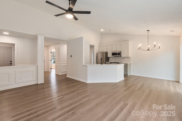 unfurnished living room featuring ceiling fan with notable chandelier, vaulted ceiling, and light hardwood / wood-style floors