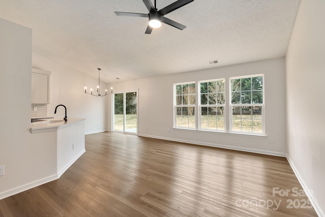 unfurnished living room featuring dark hardwood / wood-style flooring, sink, ceiling fan with notable chandelier, and a textured ceiling