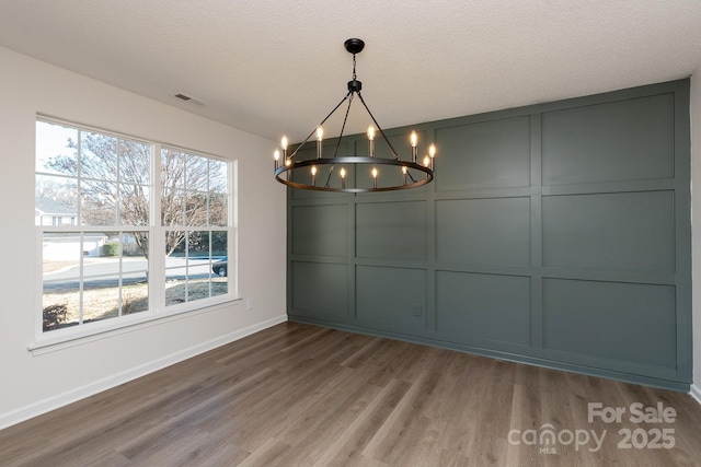 unfurnished dining area with a notable chandelier, hardwood / wood-style floors, and a textured ceiling