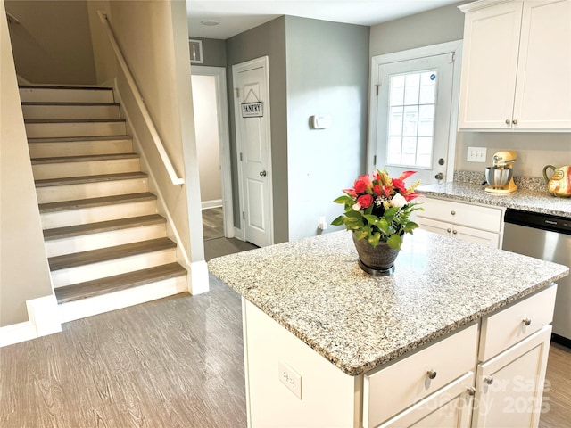 kitchen with white cabinetry, light stone countertops, stainless steel dishwasher, and light hardwood / wood-style floors