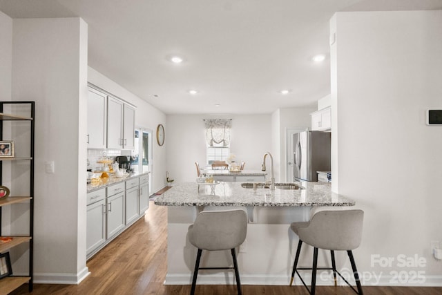 kitchen featuring a breakfast bar, sink, white cabinets, light stone counters, and stainless steel fridge with ice dispenser