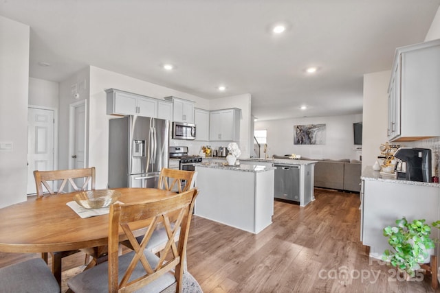 kitchen featuring light hardwood / wood-style flooring, appliances with stainless steel finishes, kitchen peninsula, a kitchen island, and light stone countertops