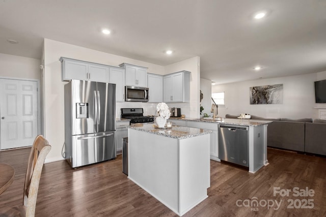 kitchen featuring sink, dark wood-type flooring, stainless steel appliances, a center island, and light stone counters