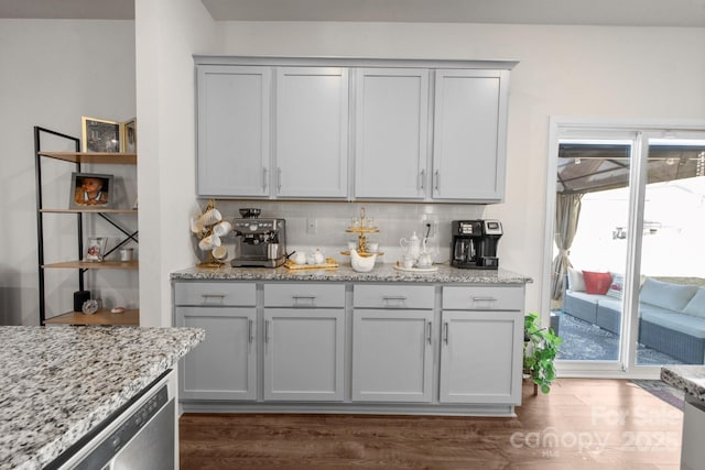 bar featuring dark wood-type flooring, gray cabinets, light stone counters, tasteful backsplash, and stainless steel dishwasher