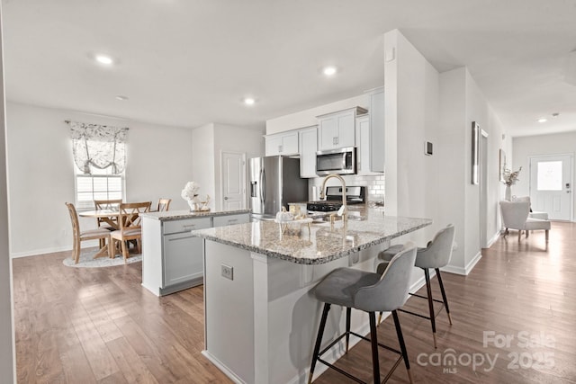 kitchen with light stone counters, hardwood / wood-style flooring, a breakfast bar area, and appliances with stainless steel finishes