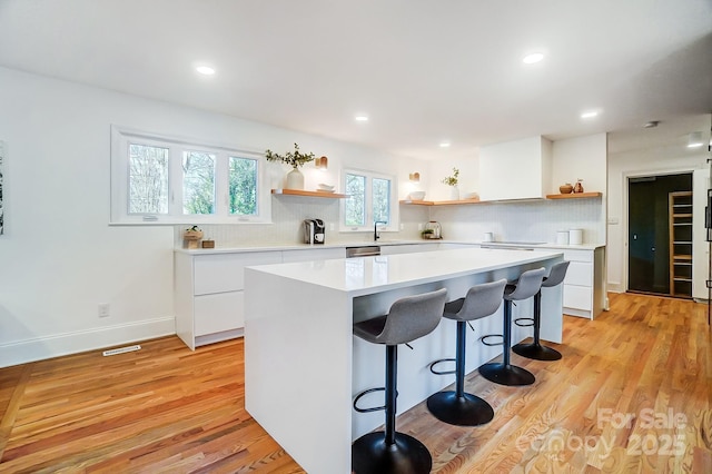 kitchen with a kitchen island, a breakfast bar, white cabinetry, backsplash, and light hardwood / wood-style flooring