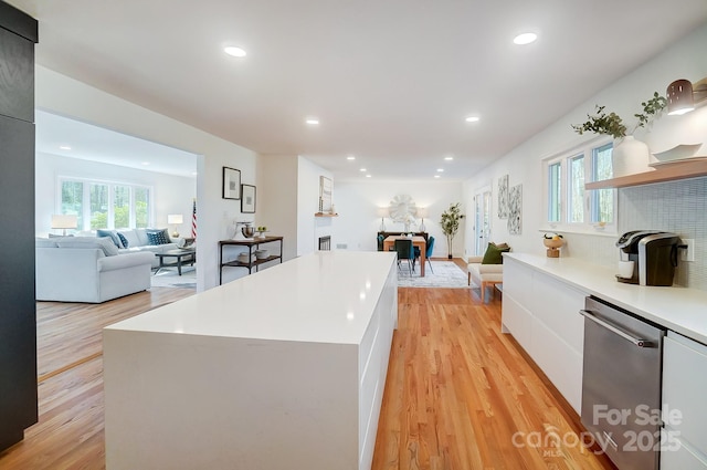 kitchen with white cabinetry, a center island, light wood-type flooring, stainless steel dishwasher, and a wealth of natural light