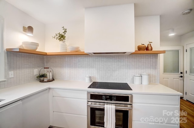 kitchen featuring black electric stovetop, decorative backsplash, oven, and white cabinets