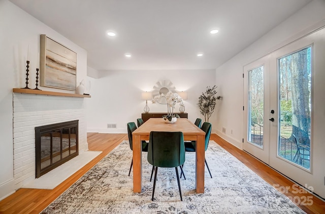 dining space with a brick fireplace, light wood-type flooring, and french doors