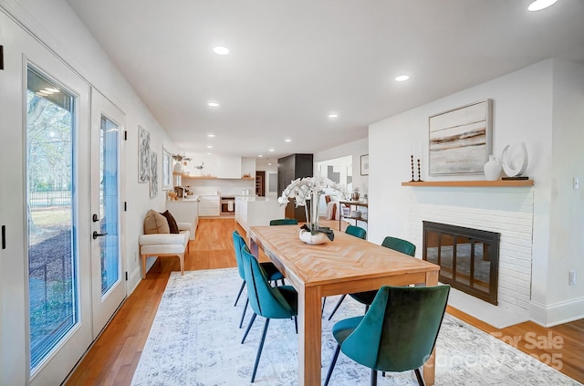 dining room featuring a brick fireplace, french doors, and light wood-type flooring