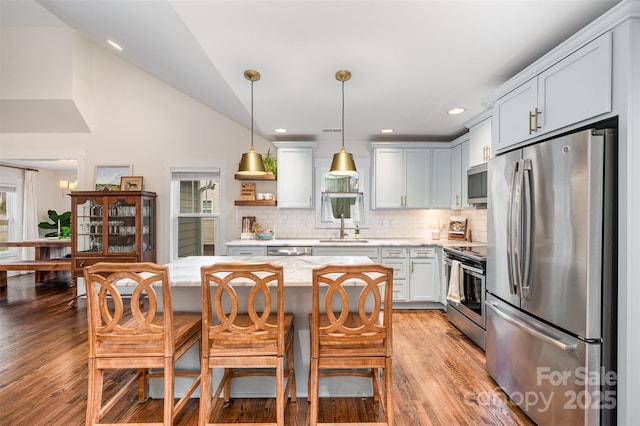 kitchen featuring sink, decorative light fixtures, a center island, stainless steel appliances, and light stone countertops