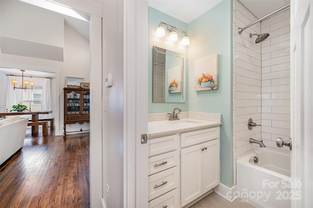 bathroom with vanity, tiled shower / bath combo, hardwood / wood-style floors, and a notable chandelier