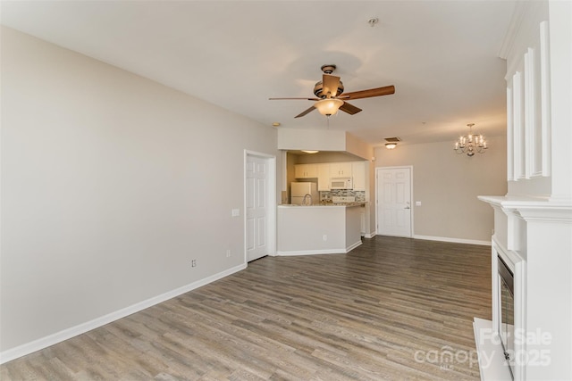 unfurnished living room featuring baseboards, wood finished floors, and ceiling fan with notable chandelier
