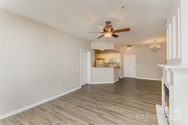 unfurnished living room with ceiling fan with notable chandelier, baseboards, and dark wood finished floors