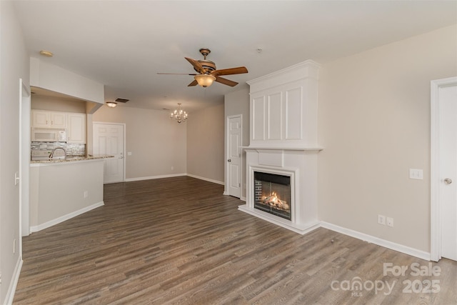 unfurnished living room featuring ceiling fan with notable chandelier, a glass covered fireplace, visible vents, wood finished floors, and baseboards