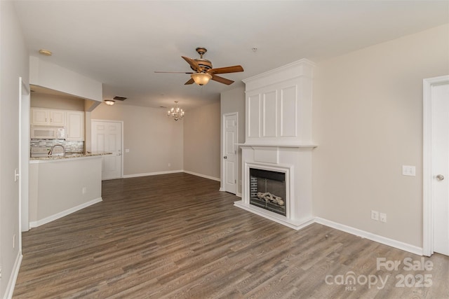 unfurnished living room featuring baseboards, a fireplace, visible vents, ceiling fan with notable chandelier, and wood finished floors