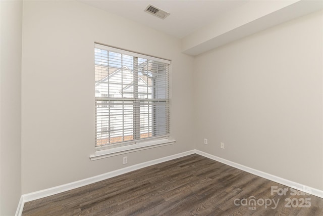 spare room featuring dark wood-style flooring, visible vents, baseboards, and a healthy amount of sunlight
