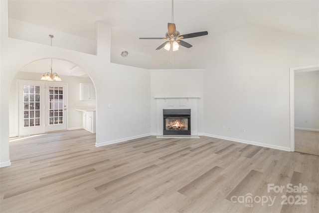 unfurnished living room with lofted ceiling, ceiling fan with notable chandelier, and light hardwood / wood-style floors