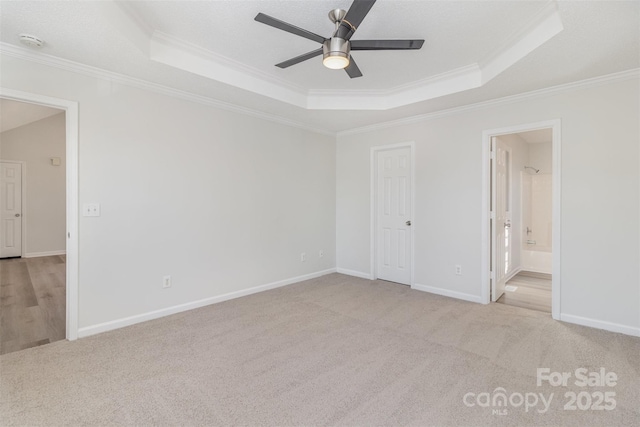 unfurnished bedroom with crown molding, ceiling fan, ensuite bathroom, and a tray ceiling