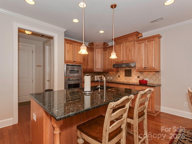 kitchen featuring tasteful backsplash, crown molding, a center island with sink, dark hardwood / wood-style floors, and pendant lighting