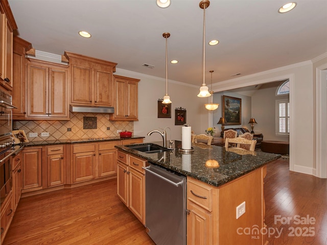 kitchen with sink, hanging light fixtures, appliances with stainless steel finishes, dark stone counters, and a kitchen island with sink