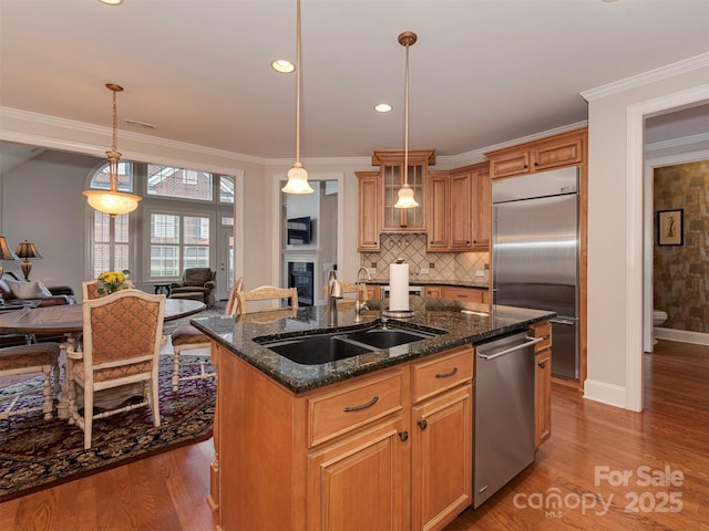 kitchen featuring sink, dark stone countertops, stainless steel appliances, a center island with sink, and decorative light fixtures