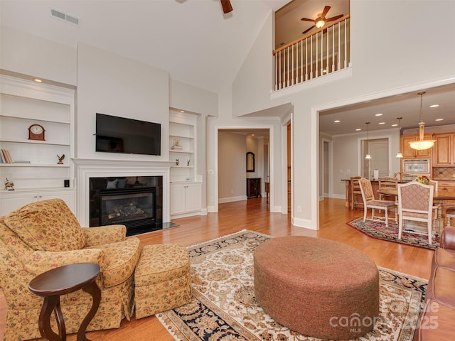 living room featuring light hardwood / wood-style flooring, built in features, high vaulted ceiling, and ceiling fan