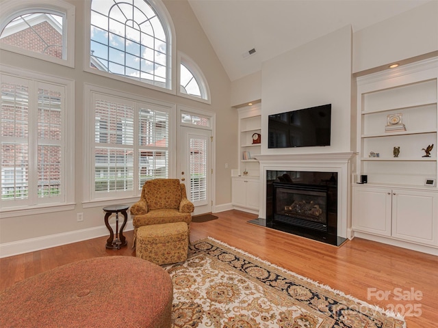 living room featuring built in shelves, light hardwood / wood-style floors, and high vaulted ceiling