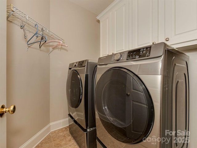 clothes washing area featuring cabinets, light tile patterned floors, and washing machine and clothes dryer