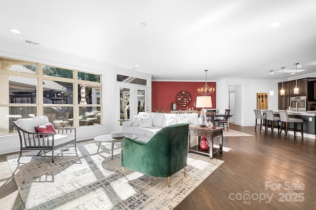 living room featuring an inviting chandelier, ornamental molding, and dark hardwood / wood-style floors