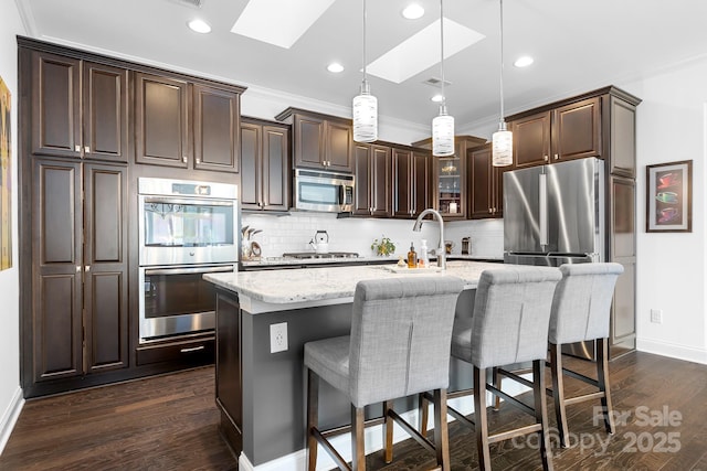 kitchen with crown molding, appliances with stainless steel finishes, a kitchen island with sink, and pendant lighting