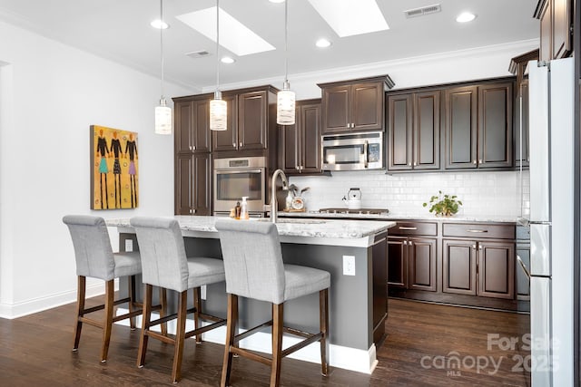 kitchen featuring pendant lighting, ornamental molding, appliances with stainless steel finishes, and a center island with sink