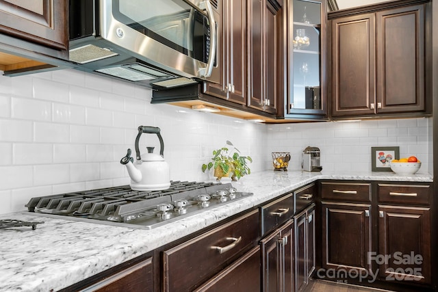 kitchen with backsplash, dark brown cabinets, light stone countertops, and appliances with stainless steel finishes