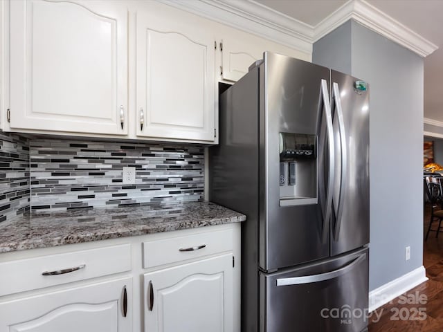 kitchen featuring crown molding, backsplash, stainless steel refrigerator with ice dispenser, white cabinets, and dark stone counters