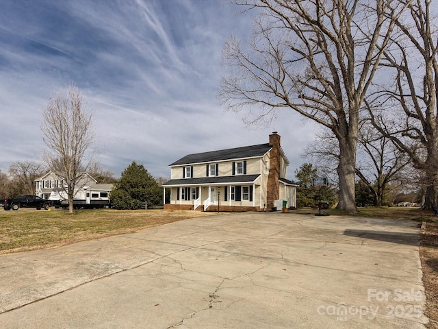 view of front of property with a front lawn, a porch, concrete driveway, brick siding, and a chimney