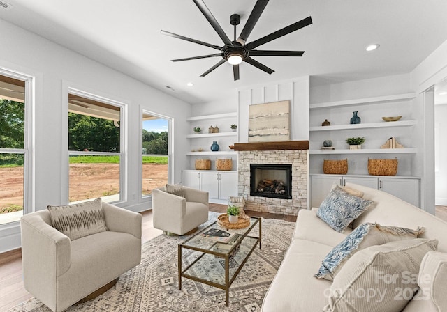 living room with ceiling fan, a stone fireplace, light hardwood / wood-style floors, and built in shelves