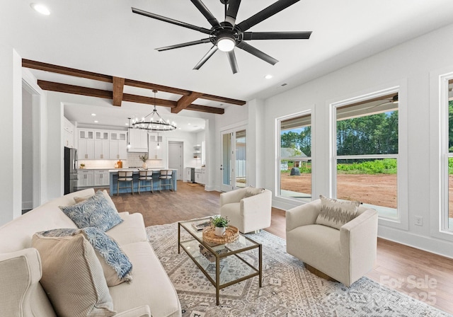 living room with beamed ceiling, ceiling fan with notable chandelier, and light hardwood / wood-style flooring