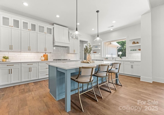 kitchen featuring premium range hood, decorative light fixtures, white cabinetry, a center island, and gas stovetop