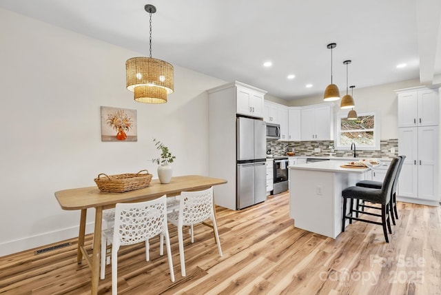 kitchen featuring pendant lighting, white cabinetry, stainless steel appliances, and a center island